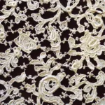 Close-up of intricate ivory lace fabric with floral and scroll patterns on a dark background