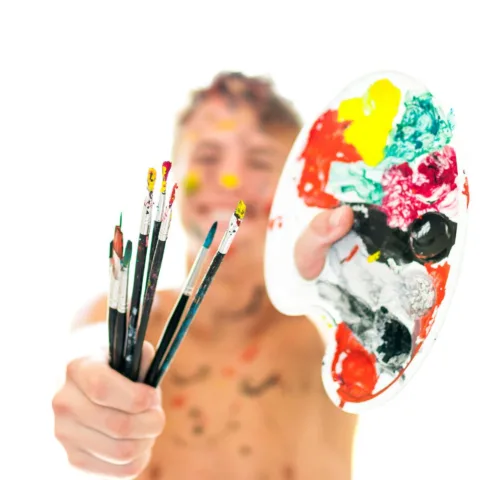 Image of a young person holding paint brushes and paint mixing palette