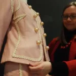 Rachel Whitworth, Curator of Fashion & Textiles adjusts pink Moschino suit