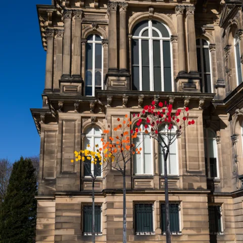 Three metal tree art installations with coloured discs outside of a historic French-style museum