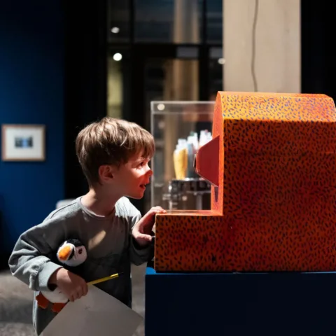 Image of a child looking at a kids automata from Cabaret Mechanical Theatre whilst holding a puffin teddy