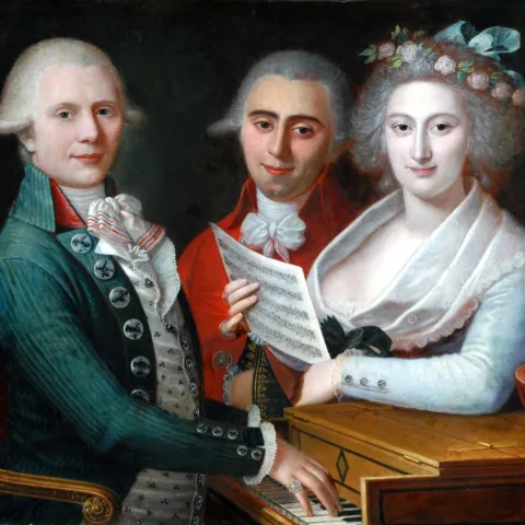 Image of a 18th century painting by Vincenzo Vita titles A Musical Party. This showcases 3 people gathered around a piano and looking at the viewer.
