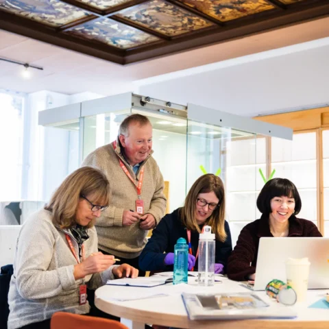 A group of people sitting around a table in a Museum gallery, working collaboratively on a research project.