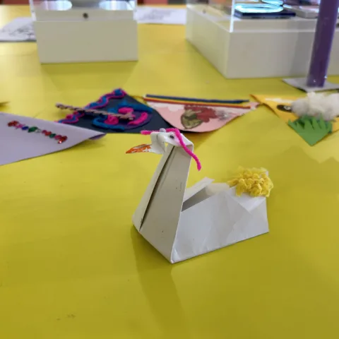 Origami swan made from paper and decorated with mixed-media materials on a desk in a museum gallery