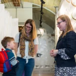 Two women with a young boy in conversation in a museum storage room.
