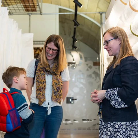 Two women with a young boy in conversation in a museum storage room.