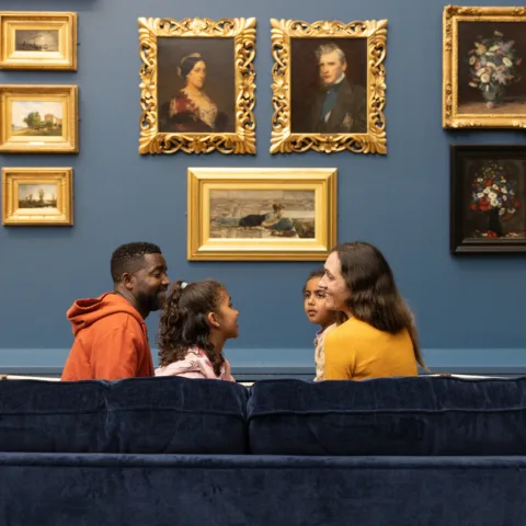 Mum and dad with two young girls, sitting on a blue couch in a museum gallery.