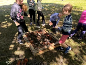 Children playing outside on grass, building a hedgehog house from natural materials.