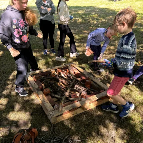 Children playing outside on grass, building a hedgehog house from natural materials.