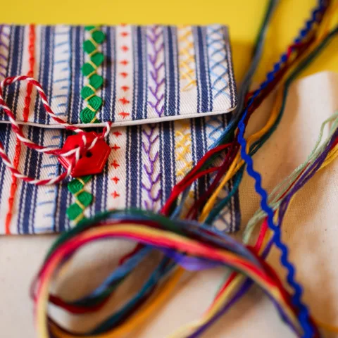 Small bag made of cotton and patterned with various styles of needlework using multicoloured thread.