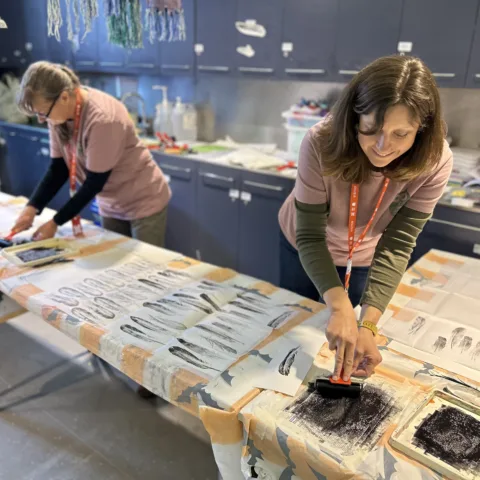 Two women printing with ink on to paper in a classroom