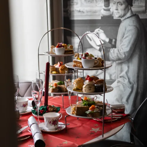 Three tiered afternoon tea, with scones, cakes and swan biscuits. The afternoon tea is on a table dressed for Christmas, with a red table cloth and silver crackers.