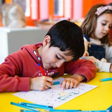 Children creating art in the create space, using pencils to colour in.