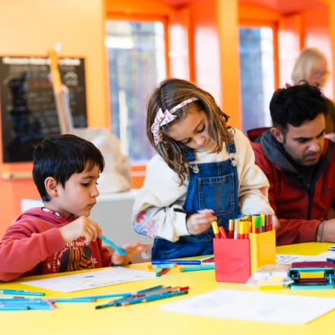 A young boy and girl working on an art project using felt tip pens to colour in.