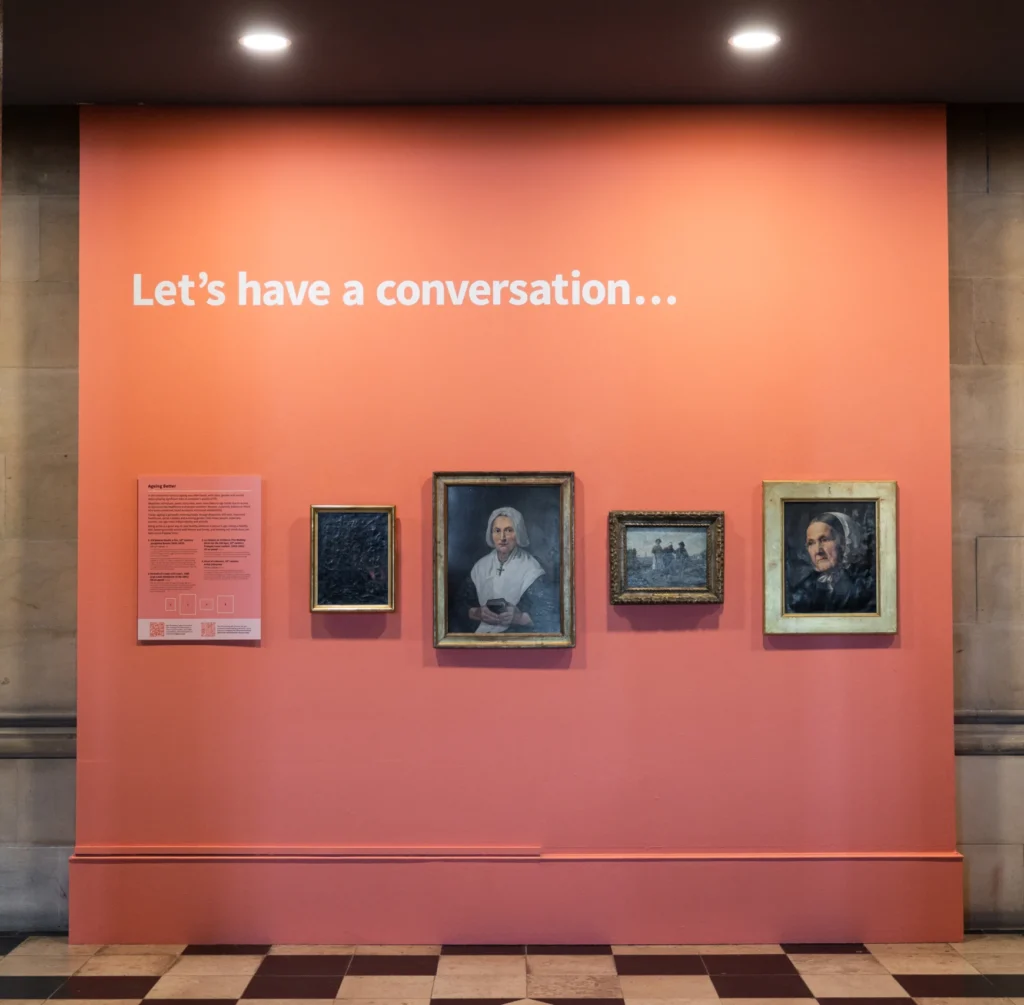 Art display on a coral wall featuring historic fine art portraits and the text, with a title, 'Let’s have a conversation...' above.