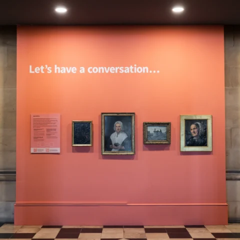 Art display on a coral wall featuring historic fine art portraits and the text, with a title, 'Let’s have a conversation...' above.