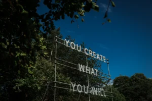 A light installation reading "YOU CREATE WHAT YOU WILL" by Nathan Coley, set against the historic Bowes Museum grounds.