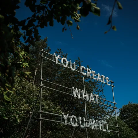 A light installation reading "YOU CREATE WHAT YOU WILL" by Nathan Coley, set against the historic Bowes Museum grounds.
