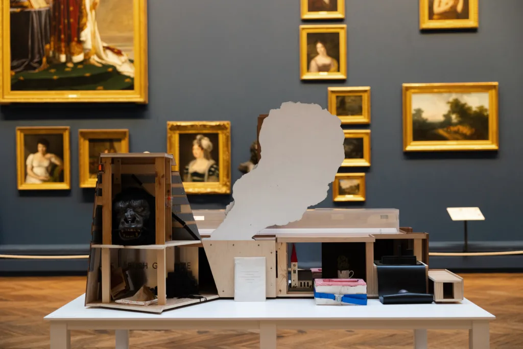 Nathan Coley’s model of the Tate Modern appears to billow smoke, creating the illusion of fire, displayed in a gallery surrounded by traditional paintings.