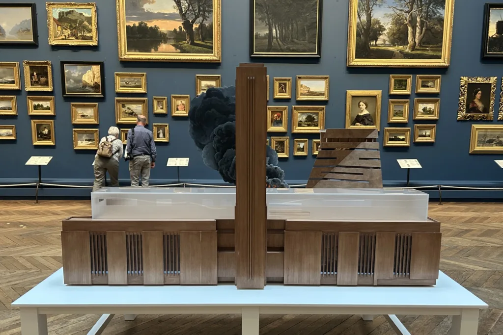 Nathan Coley’s model of the Tate Modern appears to billow smoke, creating the illusion of fire, displayed in a gallery surrounded by traditional paintings.
