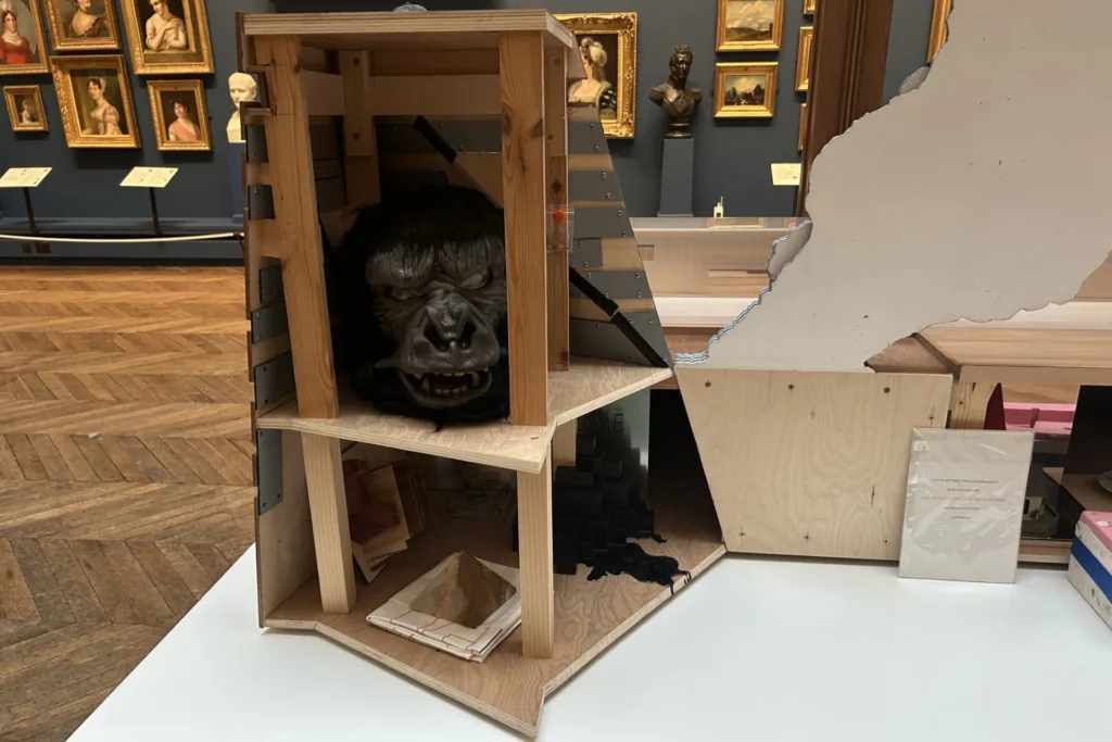 Nathan Coley’s model of the Tate Modern appears to billow smoke, creating the illusion of fire, displayed in a gallery surrounded by traditional paintings.