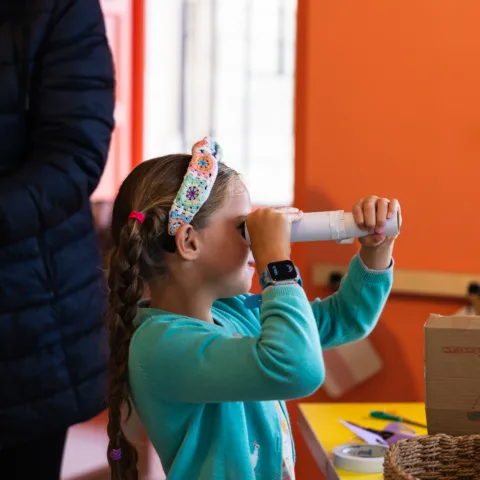 A little girl using a tube as a telescope in the create space.