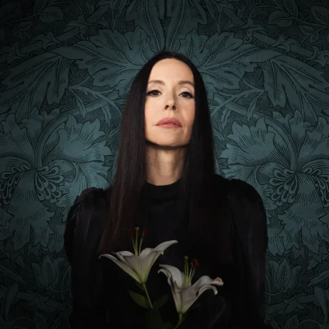 Nerina Potell holding two lillies. She has long brown hair and is wearing black clothes.