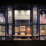 A large display case in an art gallery, showing historic embroideries and other items at different levels