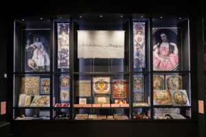 A large display case in an art gallery, showing historic embroideries and other items at different levels