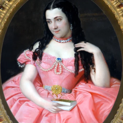 A portrait painting of a woman, Joséphine Bowes, in a voluminous pink gown adorned with pearls, a jewelled belt and a diamond necklace, holding a small book while gazing to the side with a gentle smile.