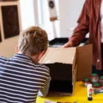 A boy wearing a striped t-shirt, putting items in a cardboard box.