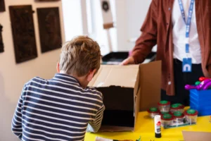 A boy wearing a striped t-shirt, putting items in a cardboard box.