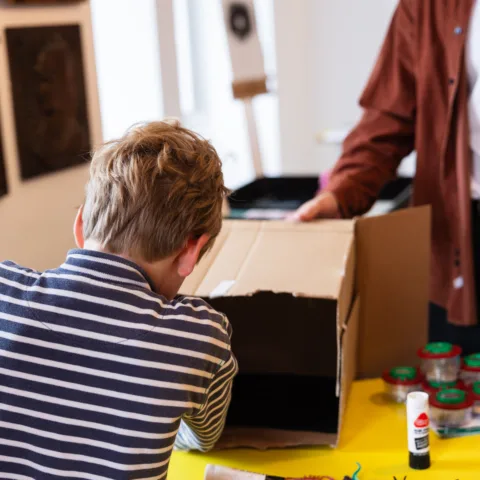 A boy wearing a striped t-shirt, putting items in a cardboard box.