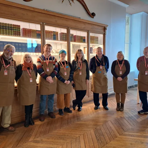 A group of volunteers wearing matching brown aprons and orange lanyards smiling in the Hive