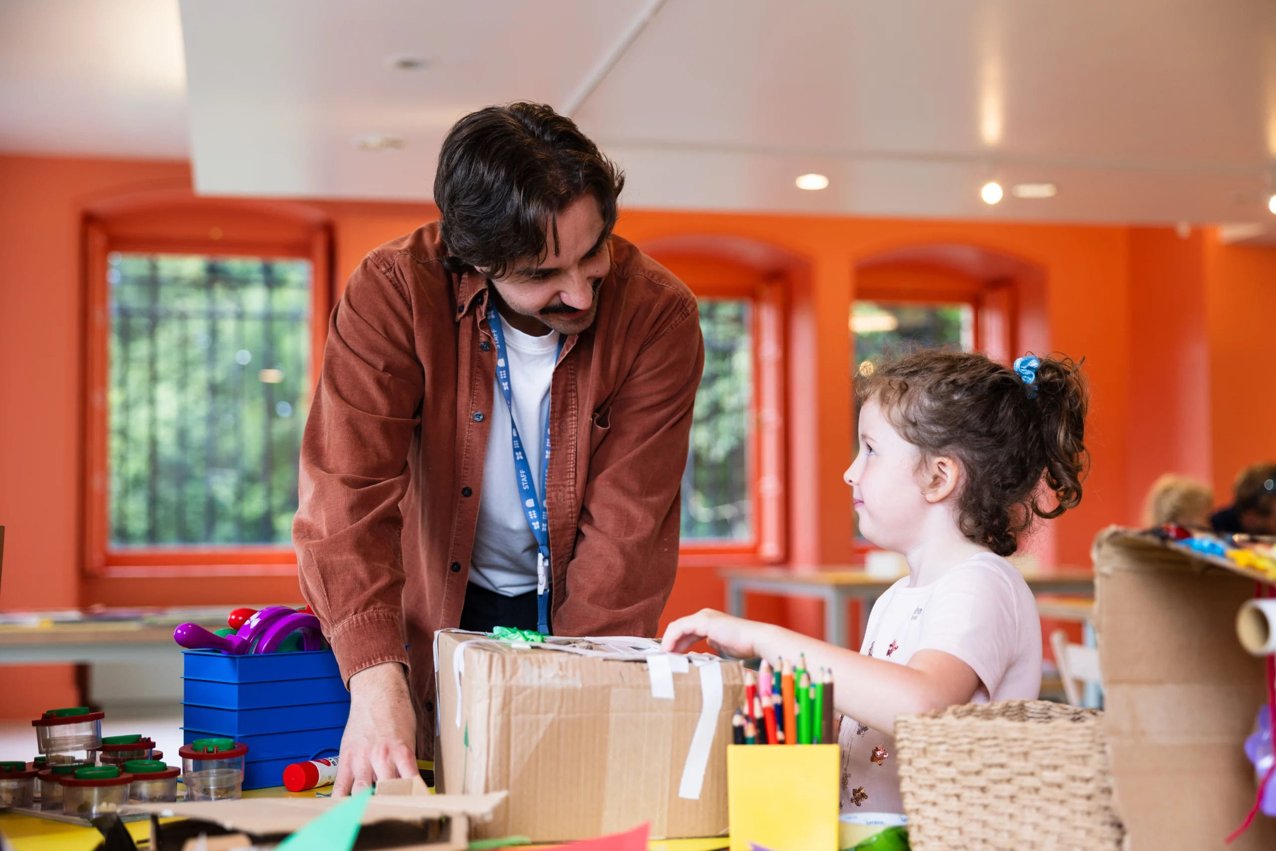 A young male staff member helping a little girl in an artist makers session 