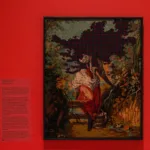 Framed needlework artwork titled 'Study in Pink and Gray by Matt Smith' is displayed against a vivid pink wall, featuring a classical pastoral scene with a pixelated grid obscuring the upper portion.
