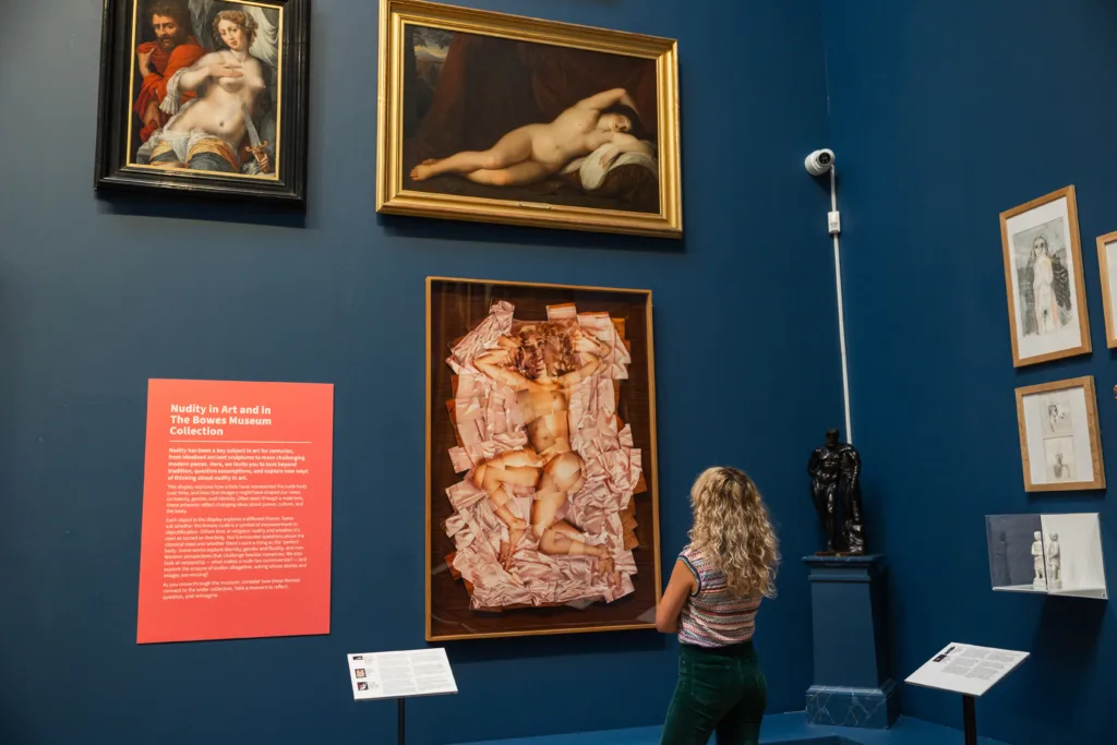 A young woman gazes thoughtfully at a painting in the Not Just Nude display in the blue picture gallery.