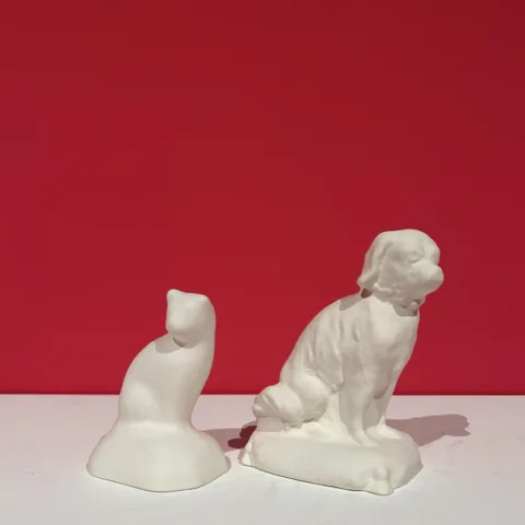 An example of a cat and dog bisque figurine against a pink background
