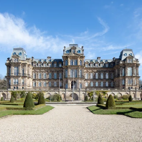 The front facade of The Bowes Museum, a grand historic building bathed in bright sunlight under a clear blue sky.