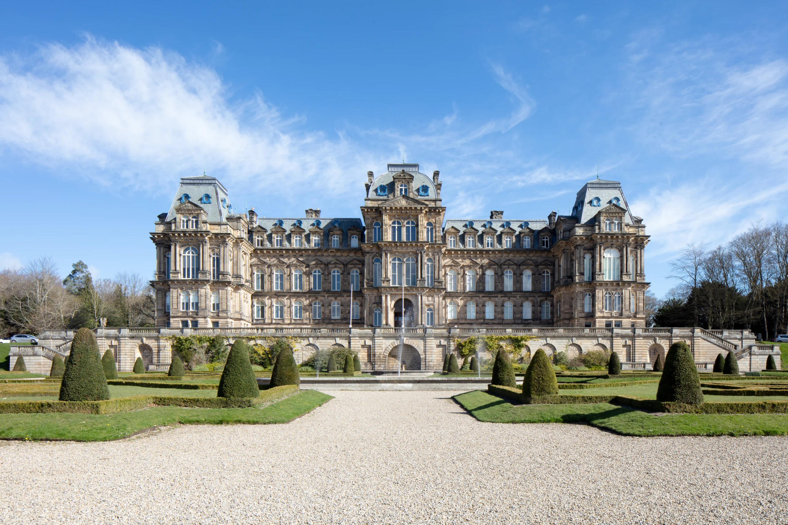 The front facade of The Bowes Museum, a grand historic building bathed in bright sunlight under a clear blue sky.