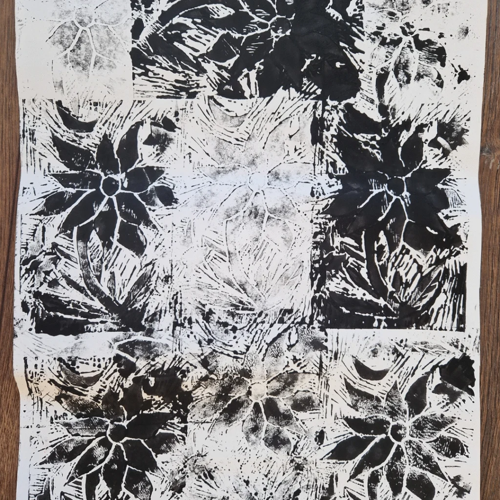 A large sheet of paper covered with repeated black-and-white block prints of floral designs. Each print features a bold flower with pointed petals and leaves, arranged in a grid-like pattern with varying ink coverage.