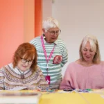 Three women in a bright gallery space doing an art workshop