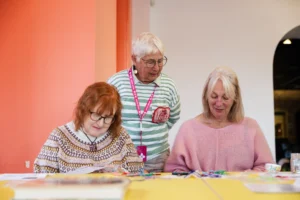 Three women in a bright gallery space doing an art workshop