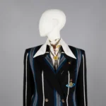 A mannequin dressed in a black double-breasted blazer with bold blue and white vertical stripes, featuring a large white collared shirt underneath. The blazer is embellished with gold buttons and two brooches—one shaped like a planet with rings and another circular pin.