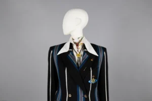 A mannequin dressed in a black double-breasted blazer with bold blue and white vertical stripes, featuring a large white collared shirt underneath. The blazer is embellished with gold buttons and two brooches—one shaped like a planet with rings and another circular pin.