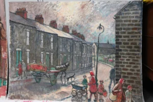 A painted street scene shows a row of grey stone terraced houses with red chimney pots lining the left side of a road. In the foreground, several figures walk along the street carrying baskets and pushing a pram, while a horse pulls a small cart with a painted sign on its side. A tall streetlamp stands near the centre of the scene. To the right, a brick wall frames the edge of the street, with more figures and buildings visible in the background. The sky is cloudy and textured, with birds flying above, and the overall palette uses muted greys, browns, and soft reds.