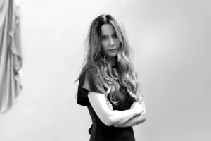Black-and-white portrait of a person standing with arms crossed against a plain background.
